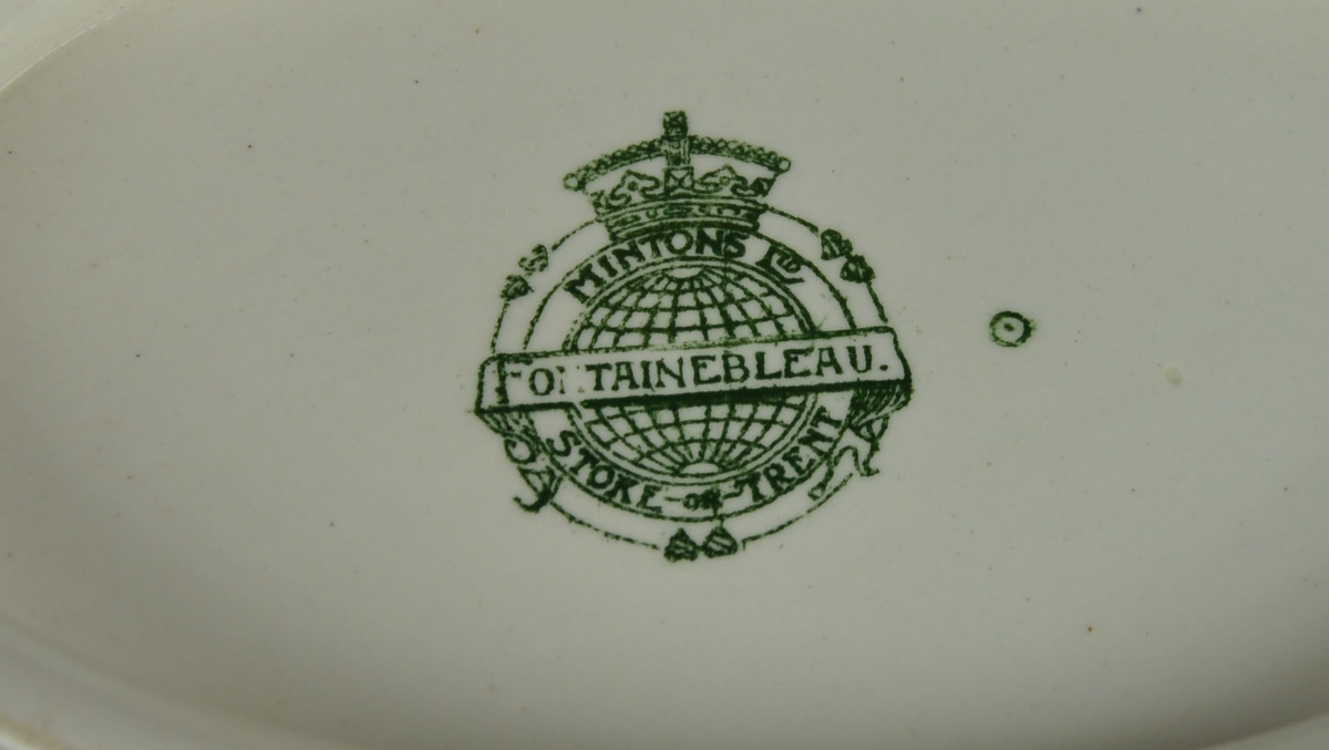 Ovalt lokkfat med tilhørende lokk og løst underfat.  Fatet har to håndtak. Det er av keramikk, steingods, med grønn bord. Borden består av eikekrans og guirlandere. Mønsteret heter Fontainebleau.