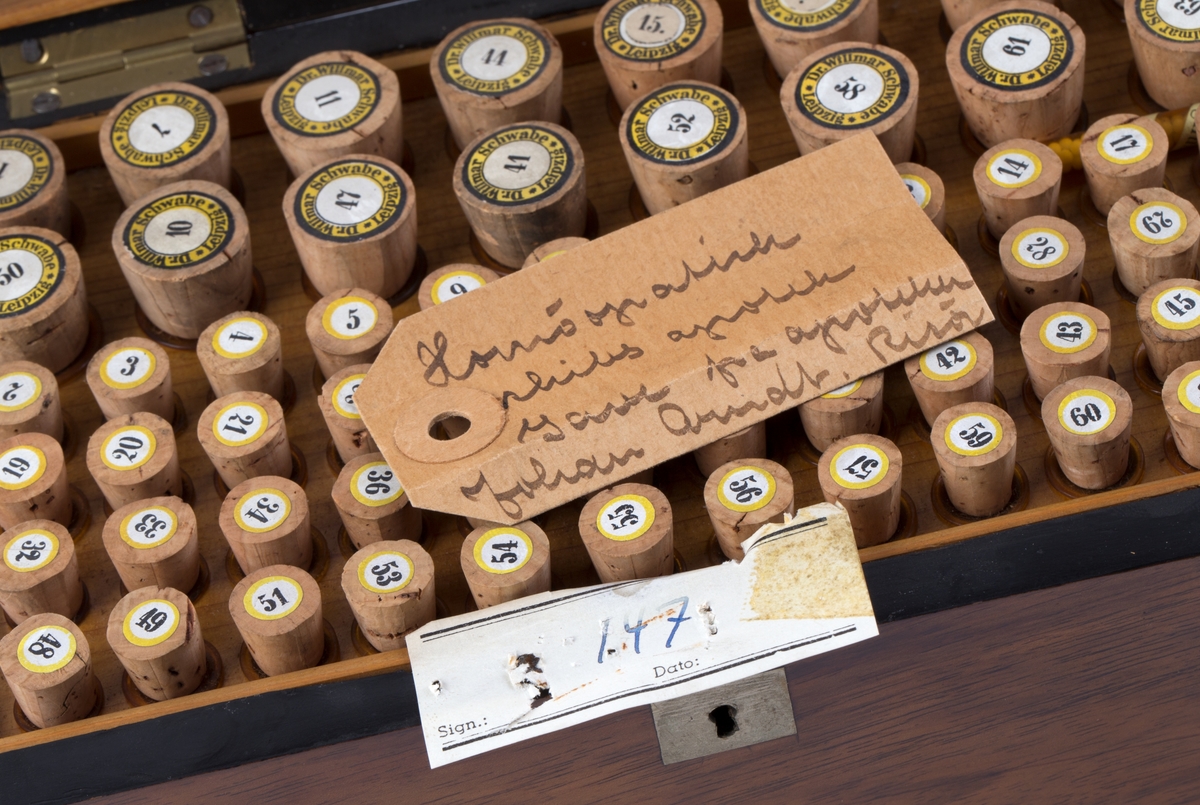 Skrin med hengslet lokk og innhold:
64 glassrør med kork påført nummer fra 1 til 64. Numrene korresponderer med plakat festet i lokket der virkestoffenes navn fremkommer. Påført nummer og navn også på hvert glassrør.