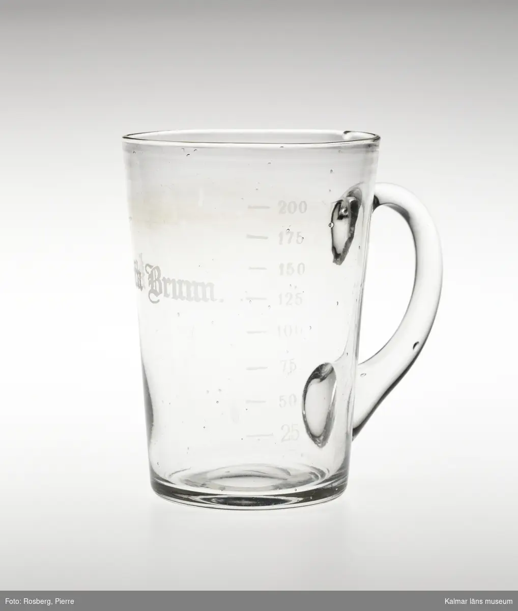 KLM 28155:1 Hankglas, av glas. Glaset är avsmalnande neråt med lodrät grepe. Slipad text, Porla Brunn och måttsticka för, 25, 50, 75, 100, 125, 150, 175, 200.