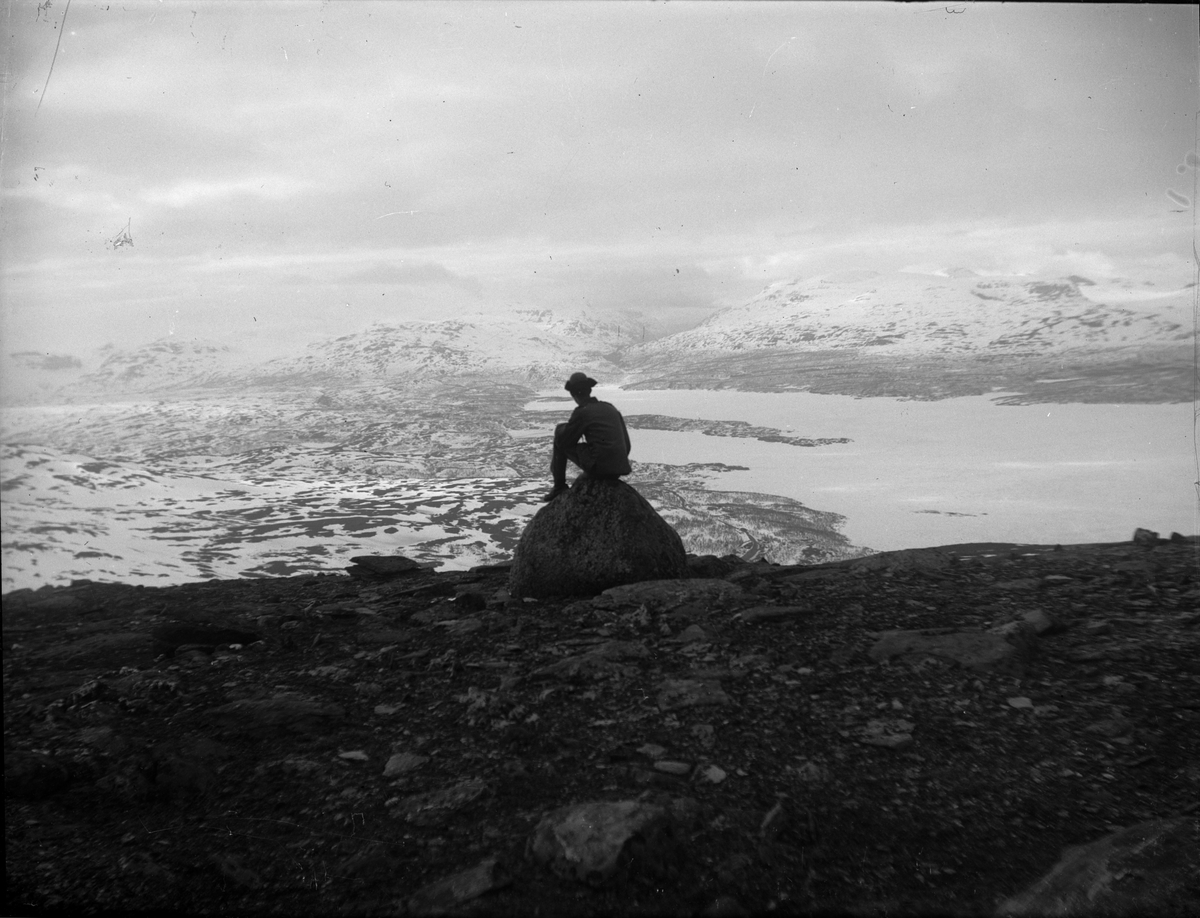 Man i uniform sitter på en sten och ser ut över fjällvy, Sverige