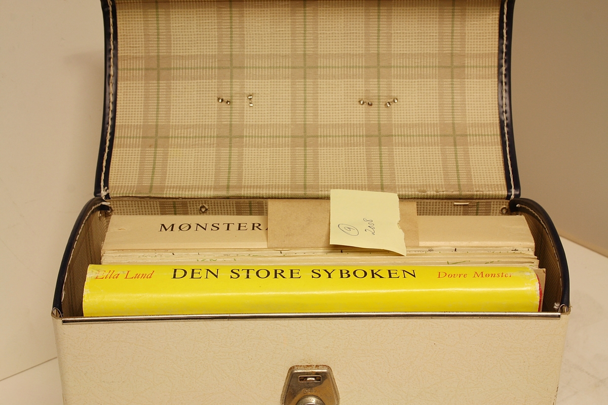 Rektangulær, stående koffert. Lokk, håndtak og lås. Innhold: "Den Store Norske Syboken" Dovre Mønster. Forfatter: Ella Lund. To holdere med mønsterark (1-21 og 22-42).