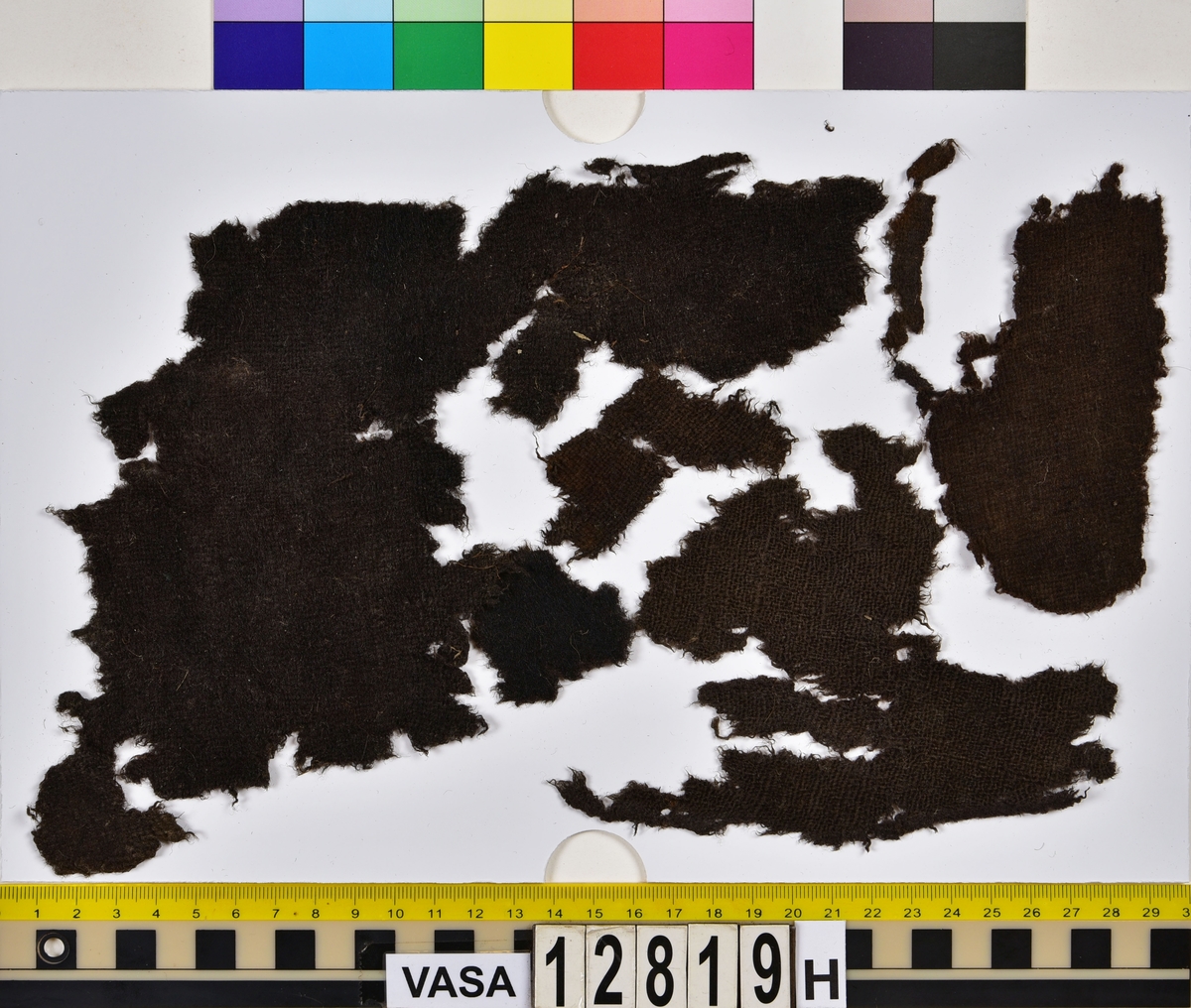 Textilfragment.
34 textilfragment uppdelade på fyndnummer 12819a-h.
Fnr 12819a består av 7 filtade fragment av ull eller bäver.
Fnr 12819b är ett vävt och valkat fragment av ull.
Fnr 12819c är ett fragment av ull vävt i 2/1-kypert samt valkat på ena sidan.
Fnr 12819d består av fyra fragment av ull vävda i tuskaft. Ett av fragmenten har en tydlig originalkant bevarad.
Fnr 12819e består av ett fragment av ull vävt i tuskaft.
Fnr 12819f består av 10 fragment av ull vävda i tuskaft. Ett av fragmenten har en tydlig originalkant bevarad.
Fnr 12819g är två fragment av ull vävda i 2/1-kypert. 
Fnr 12819h består av 8 fragment av ull vävda i tuskaft. Ett av fragmenten har många vävfel (hoppor). Ett av fragmenten har en tydlig originalkant bevarad.