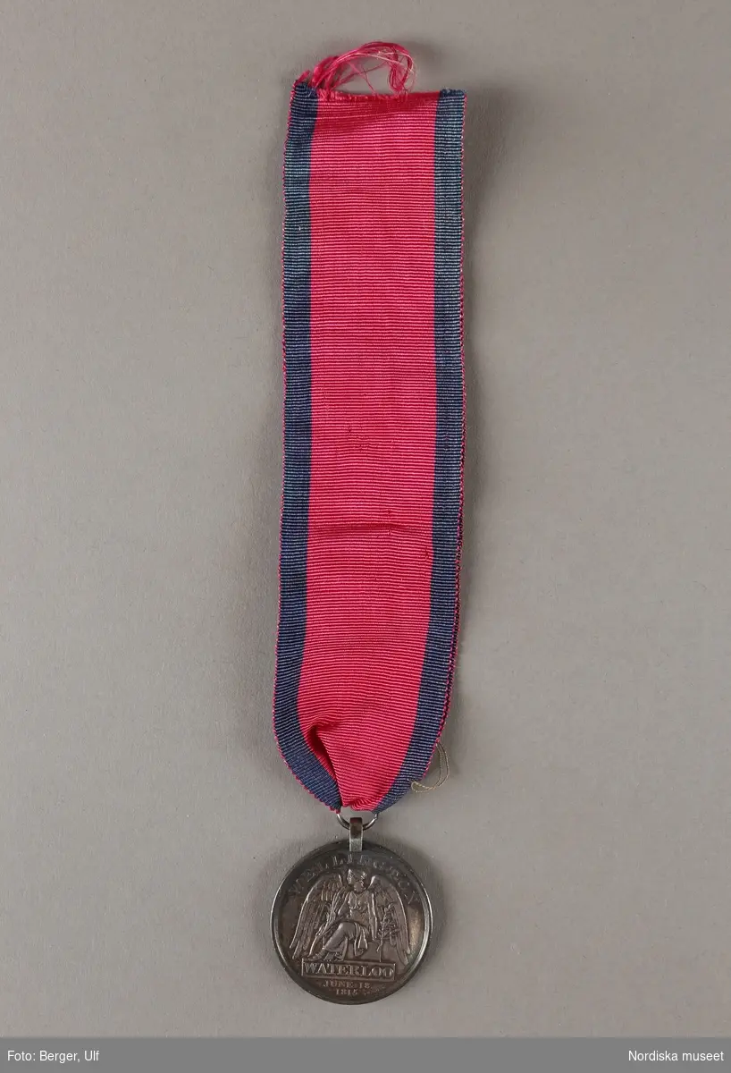 Huvudliggaren:
"Medalj. Se 34.443 [= 34.443-34.485 samlade af friherre Bennet.]
I tenn. Åtsidan: Georg IIIs bröstbild, v.s. och med omskrift: 'GEORGE P. REGENT'. Under bilden: 'T. WYON. JUN'. Frånsidan framställer segergudinnan, däröfver: 'WELLINGTON'. I afskärning: 'WATERLOO JUNE 18 1815'. Å kanten: 'JOHN SHEERMAN 2nd BATT. 59th REG:FOOT'. Diam 12 lin. 
I rödt band af sidenrips med blå ränder i kanterna.
Ink. ss. 34.424 [=ink. ss. 34.422  jämte 34.425-34.485]. [34.422=Ink. af byggmästare E. A. Boman i Stockholm 8/1 1883]"