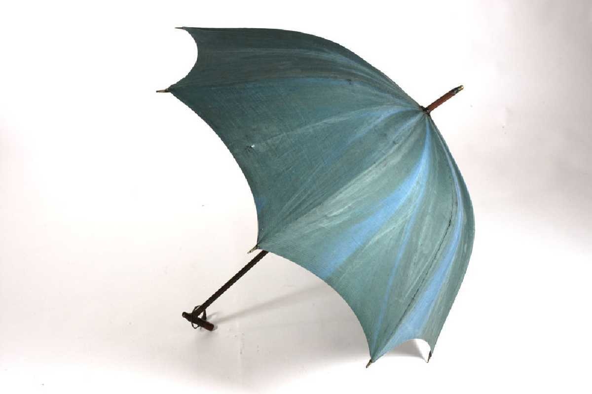 Paraplyen er lagd av bomullsstoff, lerretsbinding. 8 deler som er sydd sammen. 8 trespiler. Håndtak av tre. Malt og dekormalt, messingtupp i enden. Metallstativ for å få stoffet ut.