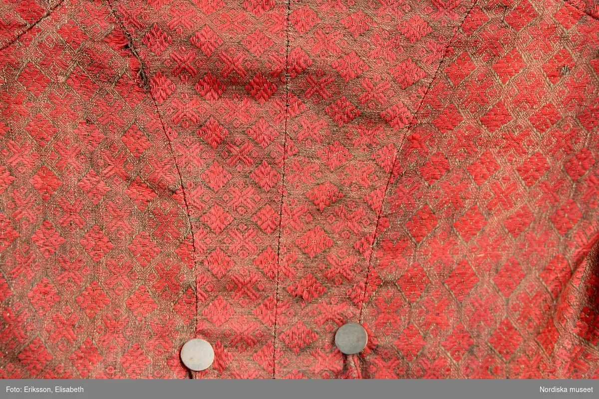 Mansdräkt (samt damdräktsdelar) antagligen från Hedebo bestående av:
a. Tröja
b:1 Väst
b:2 Livstycke
c. Toppmössa
d:1-2. Strumpor
e:1-6. 6 små huvor
f:1-3. 3 stora huvor

b:2 Livstycke längd 48 cm, skörtlängd 10 cm,
Av blommönstrat fint kamgarnsylle med glättad yta, botten starkt rosaröd i tuskaft med blombårder i raka rader i blå, gröna. gula och ljust violetta nyanser. Blommönstret kräver en extra mönstervarp som flotterar på baksidan och mönstret har dragits i simpelvävstol. Tyget kallas taborett.
2 framstycken, 2 sidstyvkenmed materialskarv på båda, 2 ryggstycken som avslutas bak i 2 stora skörtflikar, skörtöppningarna har förstärkningar tränsade med ljusblått lingarn. På fram-och sidstycken är skörtet av flera hopskarvade delar med 2 sprund fram med sprundförstärkningar som bak. Foder av oblekt linnelärft med fastsydda slåar med 6 par hål för dold snörning fram. Livet kantat med 2,5 cm breda klargöna ylleband som är sekundärt påsydda under 1800-talet.
Taborett av denna höga kvalitet vävdes i Norwich i England och började exporteras under 1760-talet till övriga Europa. Användes i Norden till livstycken, mansvästar-och tröjor och kjolar av förmöget bondfolk. Livstycket är antagligen från sent 1700-tal. Se även kjol inv.nr 16299 från Ålborg.
/Berit Eldvik 2006-11-23
d:1 - 2 Ett par mansstrumpor slätstickade av vitt ullgarn, kant upptill stickad med 3 aviga, 3 räta maskor.
Anm. Var utställda på Leksandsfigur i Folkdräkter 1977(?) - 2004 och blev där malätna.
/Berit Eldvik maj 2006