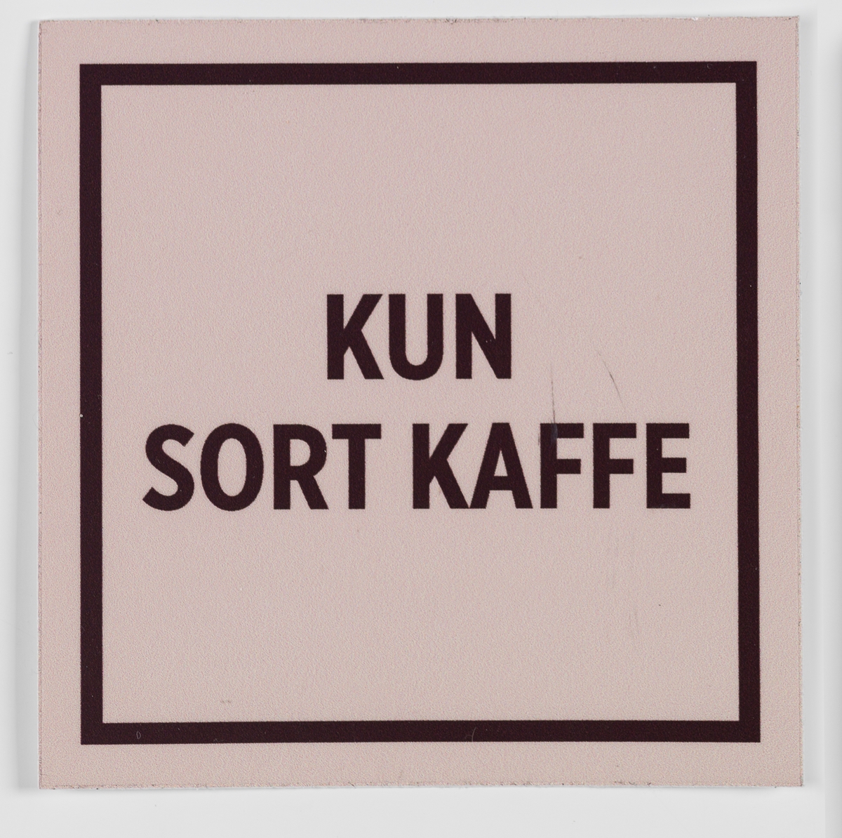 Et kvadratisk klistremerke med stilisert ramme med beige bunnfarge og brun skrift. Kan klistres på en flate i nærheten av kaffeautomaten i butikken.