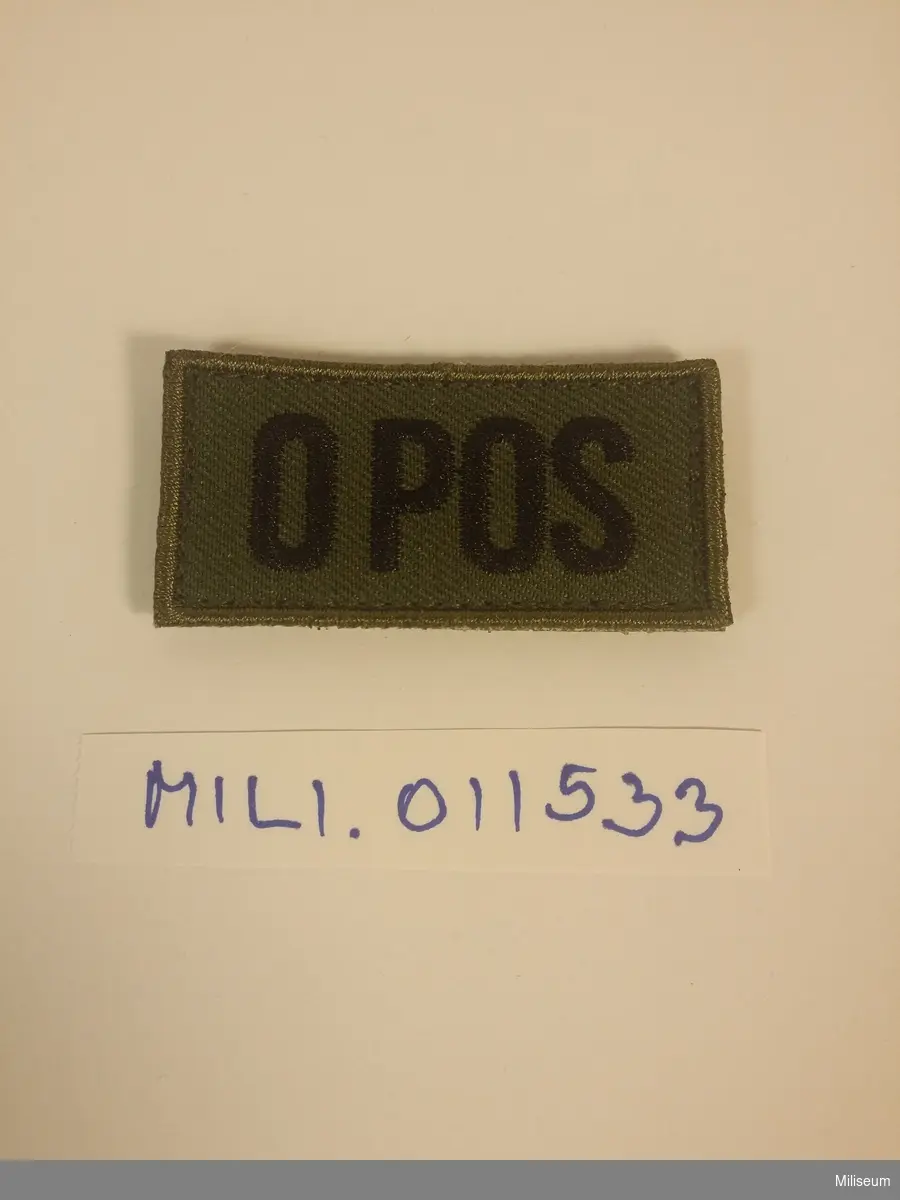 Tilläggstecken med texten "O POS". Med kardborreväv på baksidan.