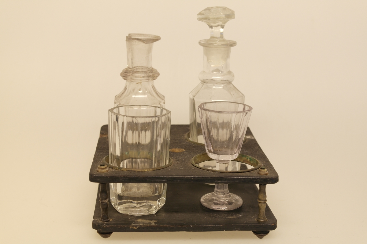 Kryddersett bestående av stativ (a), to flasker (b, c, f) og to glass (d-e).
A) Krydderstativ av tre og støpt messing. Messingkant rundt 4 sirkelåpninger. Fire balusterformede messingbein.
B) Flaske i støpt glass med glasspropp (F)
C) Flaske i støpt glass
D) Støpt glass