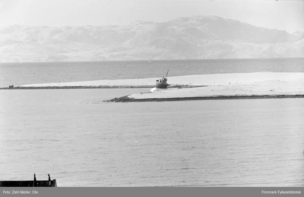 Fotoserie tatt i Vadsø i 1968 av Vadsøfotografen Ole Zahl-Mölö. Bildet viser et område på Vadsøya med en fiskebåt som ligger strandet i fjæra.