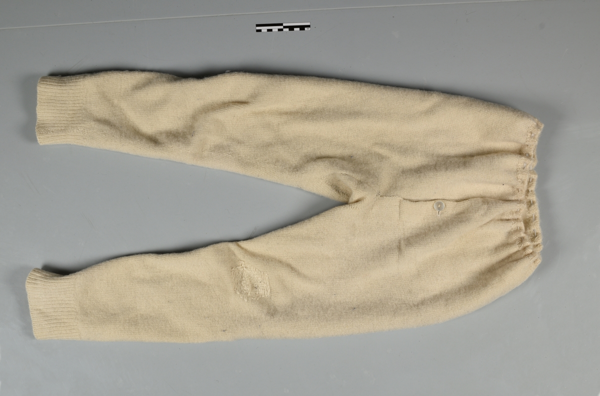 Underbukse - ull, strikket - rettstrikning, hvit, gylfhull med 1 knapp, strikk  i linning, kile i skrittet, venstre kne er stoppet. 