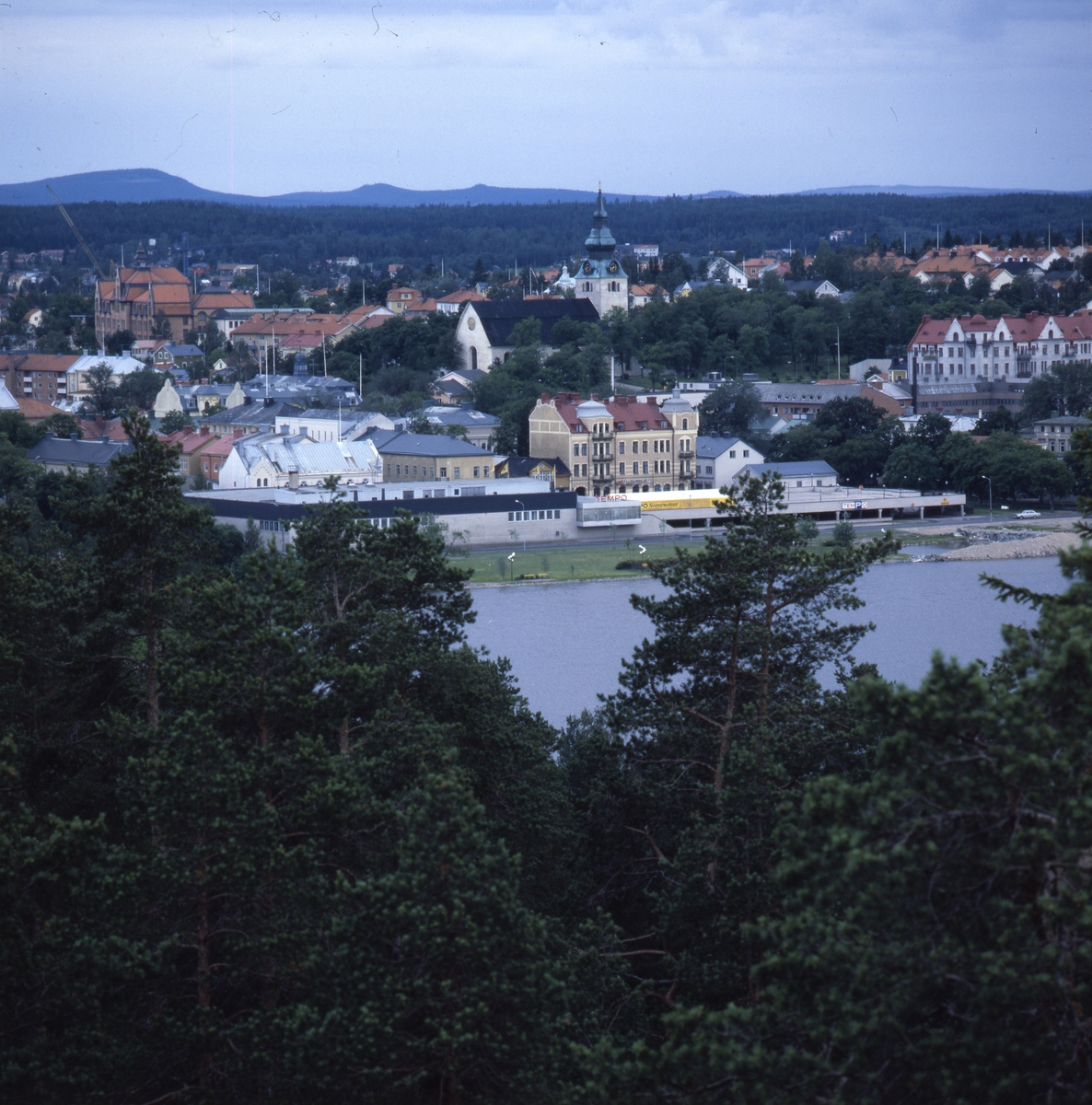 Vy över talltoppar över sjön Lillfjärden, in mot Hudiksvalls stadskärna med sin kyrka.