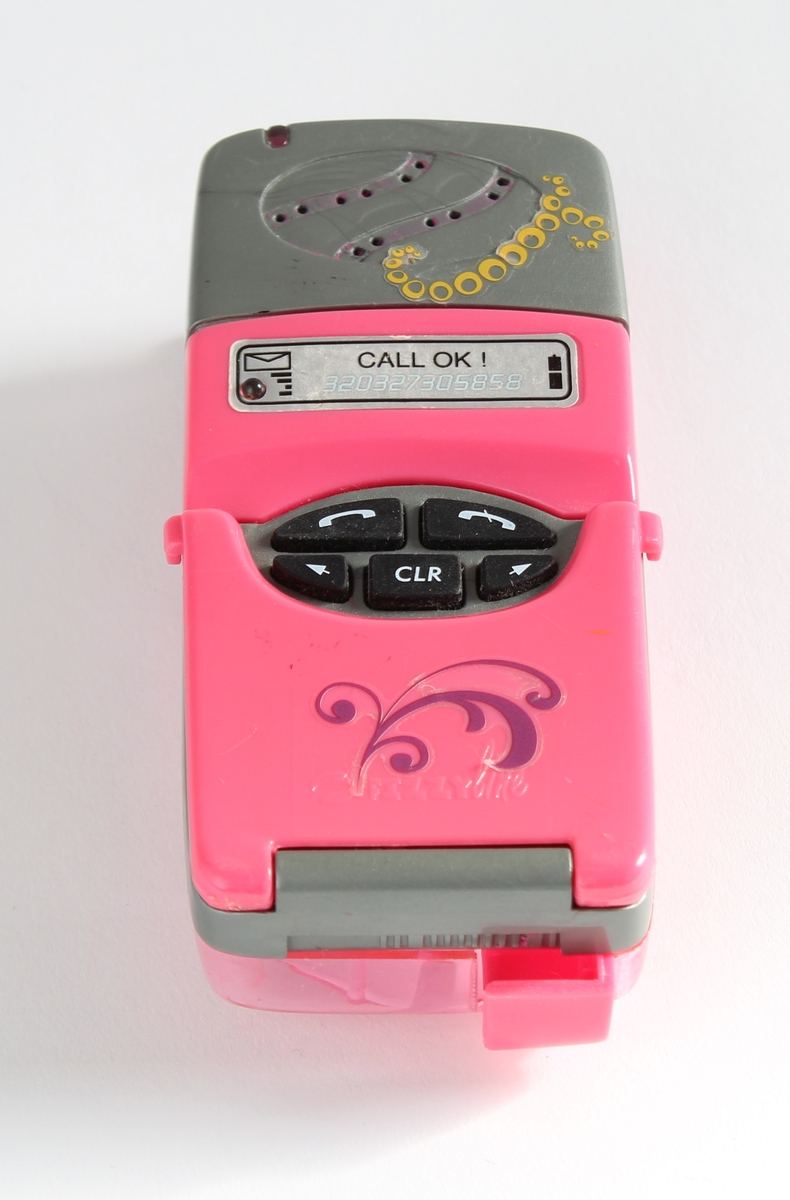 Tilhørt jente (f. 2001) i Sør-Odal. 
En rosa mobiltelefon-leke. Den er utformet som en normal mobil i størrelse. Med trykkbare taster og lokk til å åpne. Den er dekorert med en gul sommerfugl.