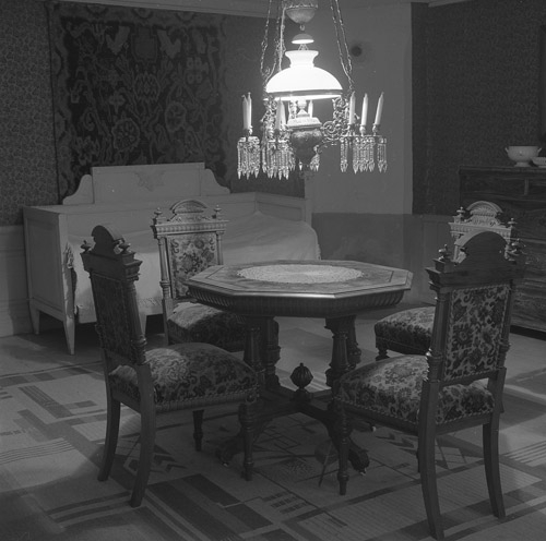 En interiörbild av en matsalsgrupp med ett runt bord med fyra stolar. Över bordet hänger en kristallkrona med glaskupa.