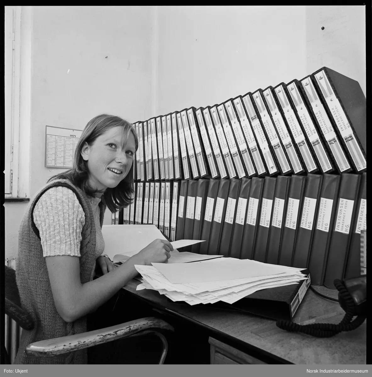 Kvinne på kontor med en samling av instruksbøker for Mg.