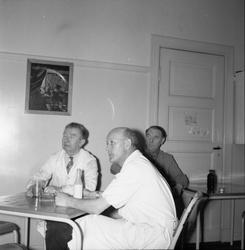 Tre menn, ein i kvit frakk på kvilerom på DNZ, Zinken,