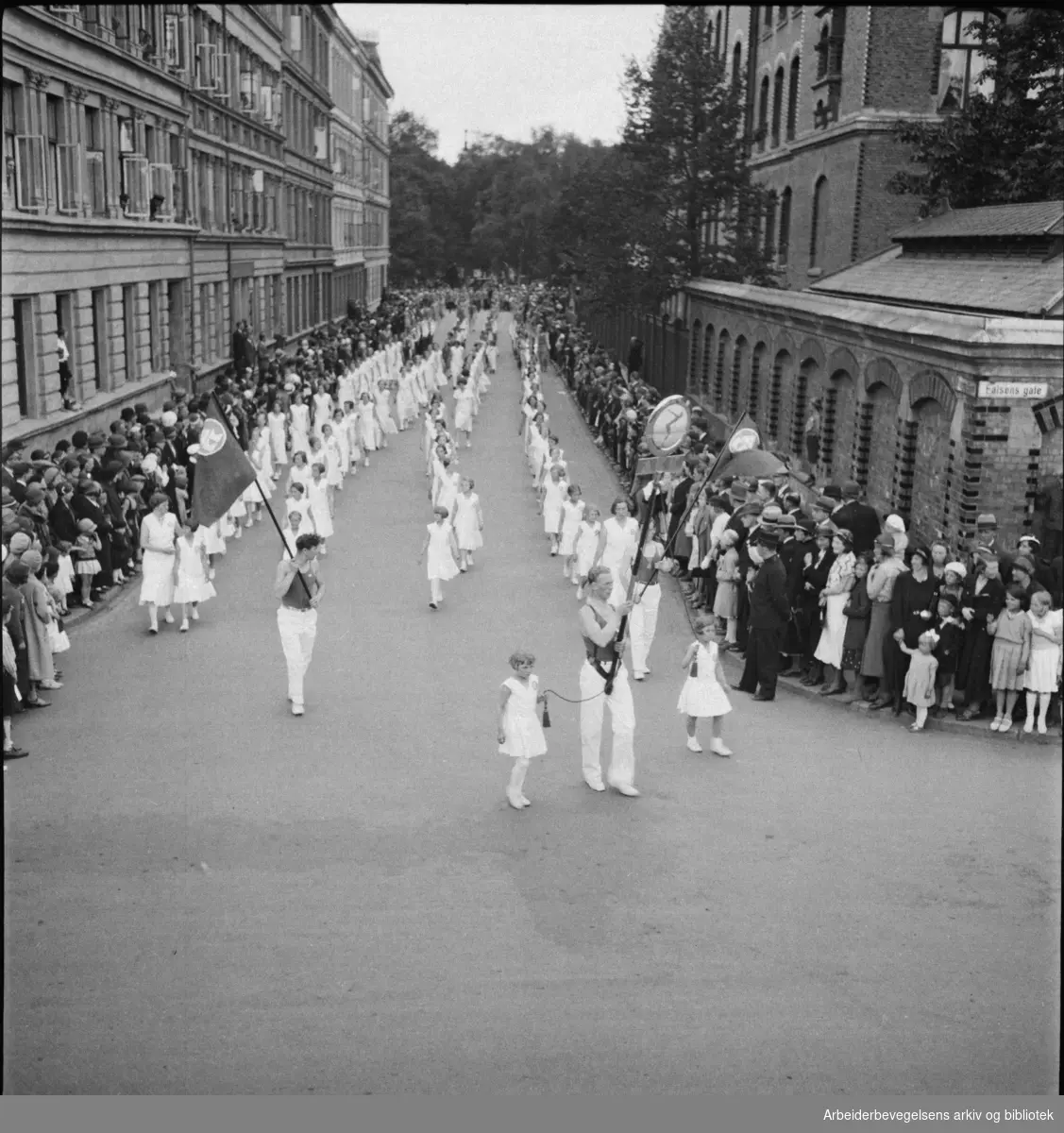 1. Mai 1932 på Dælenenga i Oslo. Medlemmer av A.K.K. (Arbeidernes Kappsvømningsklubb) Bildet er tatt på hjørnet av Falsens gate og Nissens gate, med Birkelunden i bakgrunnen. Grünerløkka skole til høyre.