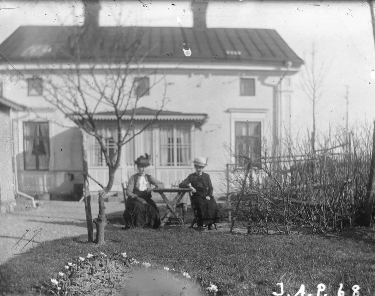 "Stora huset Kryddgårdsgatan 32 B, Sandgatan 28". Två kvinnor framför det hus som var familjen Johan August Petterssons hem fr.o.m. 1913 och framåt, Enköping. Vy från nordväst.