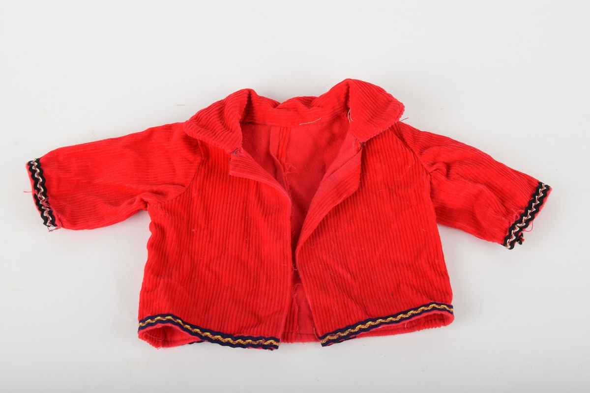 Dukkejakke med krage i rød kordfløyel. Kantene på armene, samt nedre kant av jakken, har påsydd pyntekant.