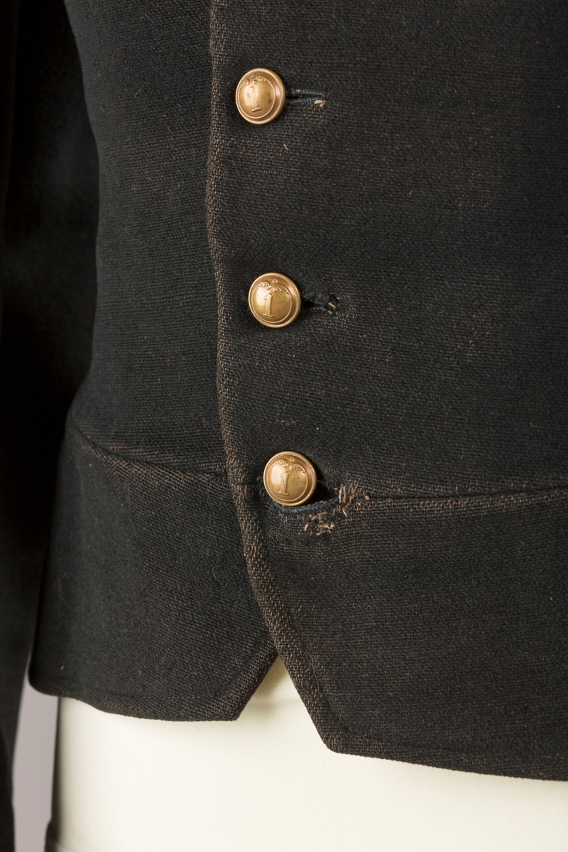 Form: Enkeltspent.

Foret med lin. Forsterket med silke på et lite stykke på ryggen. 12 messingknapper med mønster og tallet 1. Hempe i lin. Bendelbånd med knappehull.