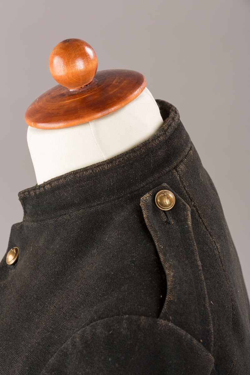 Form: Enkeltspent.

Foret med lin. Forsterket med silke på et lite stykke på ryggen. 12 messingknapper med mønster og tallet 1. Hempe i lin. Bendelbånd med knappehull.