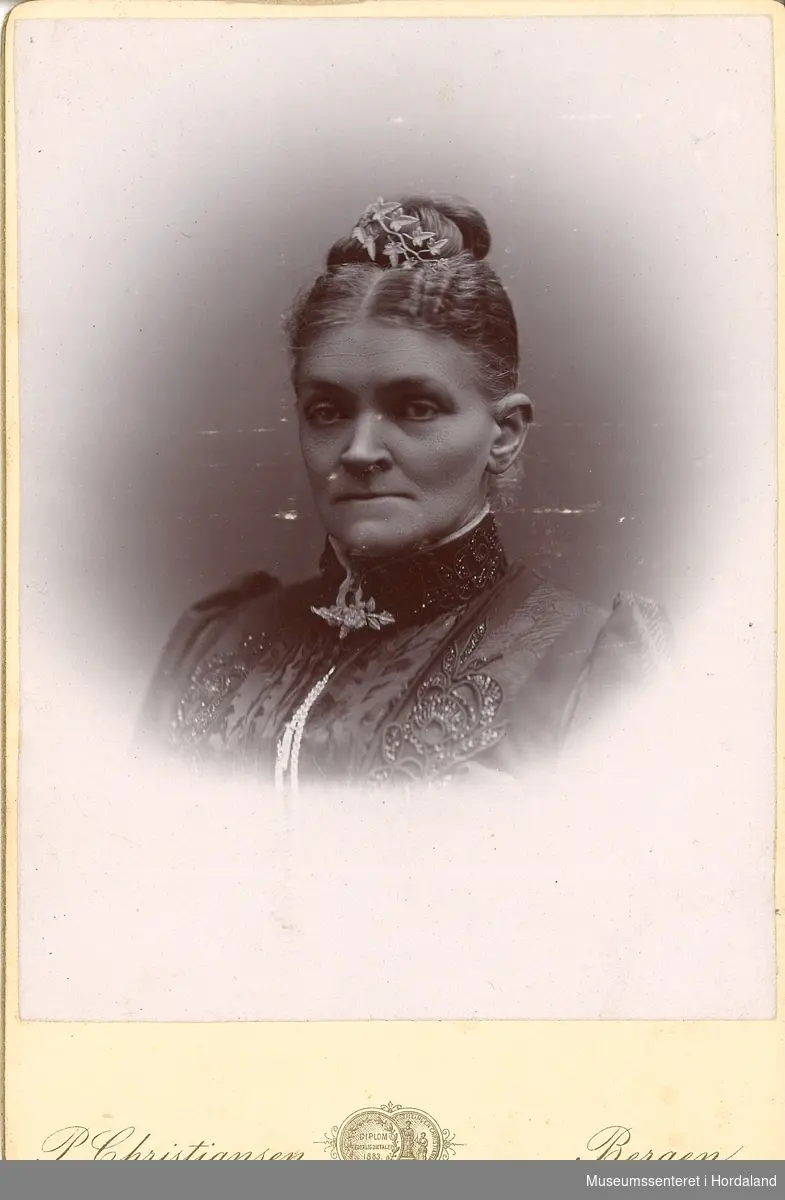 portrettfotografi av kvinne med oppsatt hår, mørk kjole med perlebroderi og bladsmykke i halsen og  håret