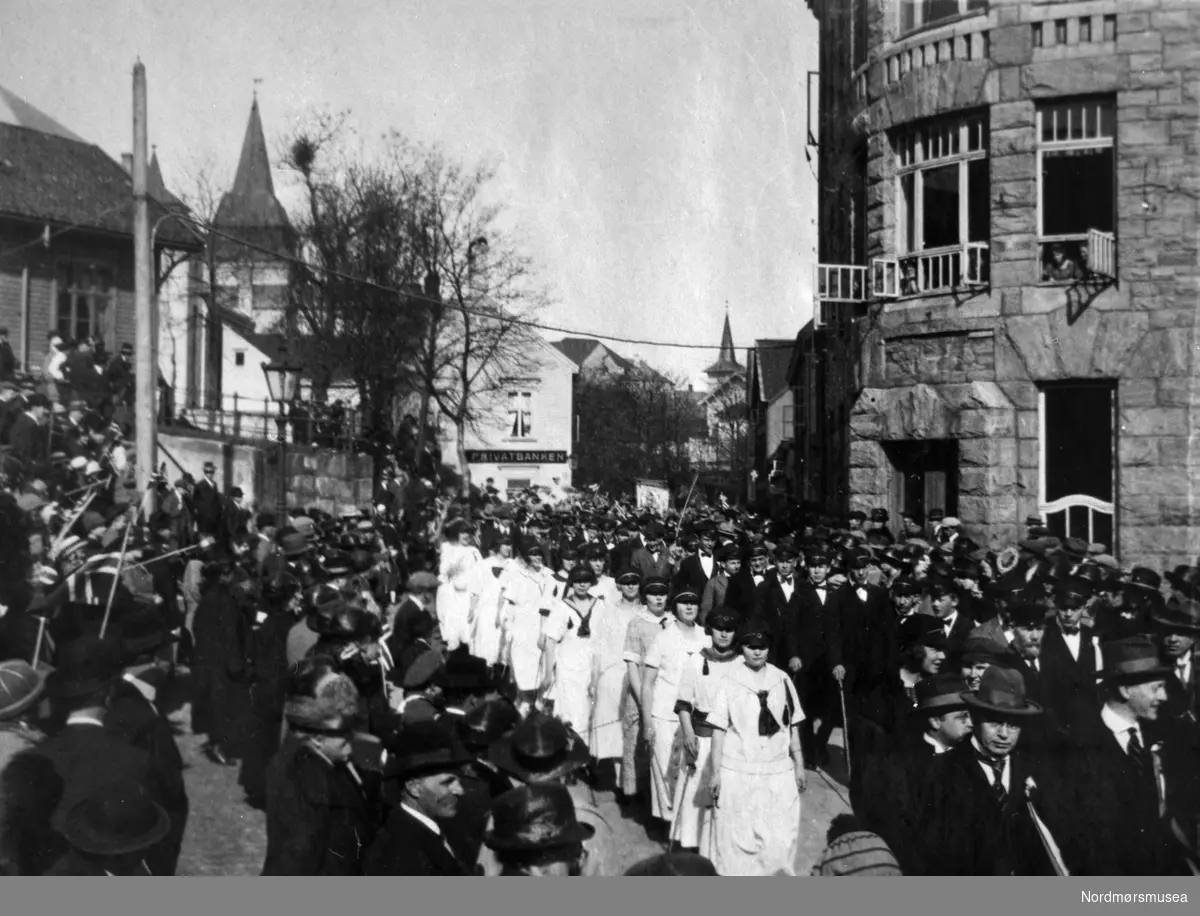 "Russen 17de mai 1924, [...]" Foto av Kristiansundsrussen på torget på Kirkelandet i Kristiansund, 17. mai 1924, Privatbanken, Kommunebygningen på Torvet. Fotograf er ukjent. Fra Nordmøre museums fotosamlinger.