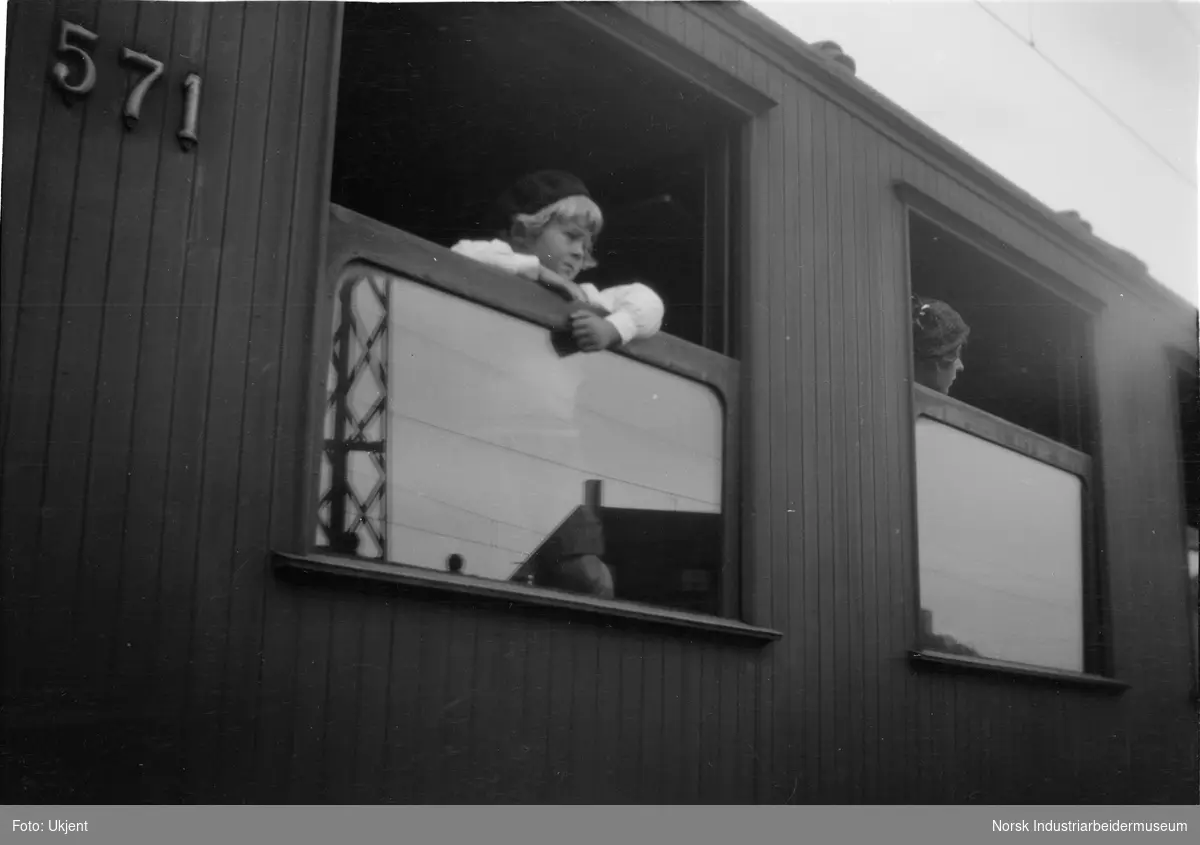Liten jente titter ut gjennom vindu i togvogn nr 571.