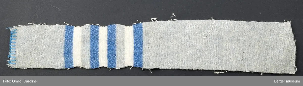 En prøve. En blå prøve er klippet av. Ensfarget gråblå med striper i mørk blå og hvit.
