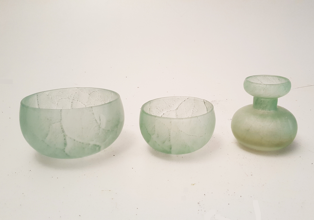 it sett med tre pyntegjenstandar; ein vase og to bollar i gjennomskinleg, lys grønt glas med ujamn farge.