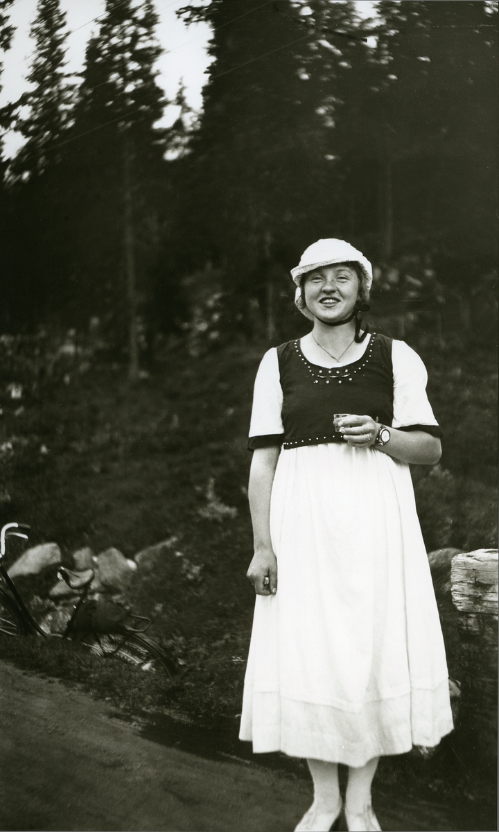 Kvinne m/pjolterglass stående på landsvegen.
Portrett av Gudrun Berg f. Bakken (1910)