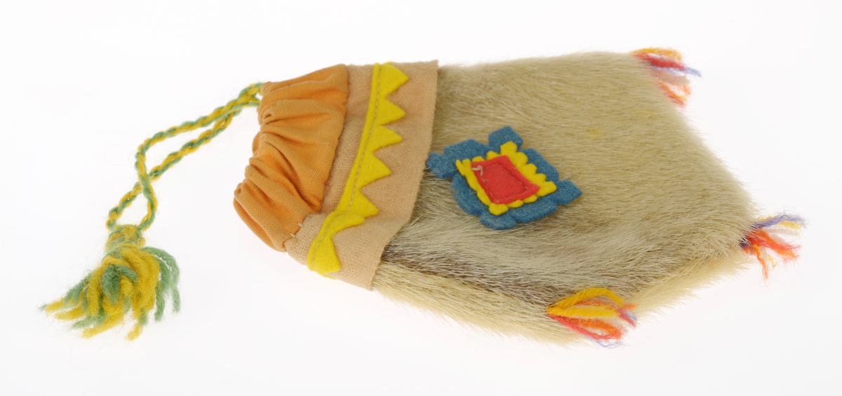 En liten veske laget av garvet reinskinn. Den er spiss i enden og har en slags ruter-form. Øverst er det sydd på en dobbel kant av oransje bomullsstoff. Gjennom denne er det tredd en tvunnet ullsnor i gult og grønt med en dusk i enden. Med snoren kan man åpne/lukke vesken. Deretter er det sydd på en stripe med lys oransje ullstoff der det er sydd på en trekantbord av gult ullstoff. På midten av vesken er det sydd på tre firkanter av filt oppå hverandre. Den nederste er blå med takkete kant, deretter er det en gul med takkete kant og til slutt er det en rød firkant. I spissene nederst på vesken er det sydd på små dusker av ullgarn i rødt, blått, hvitt og gult.