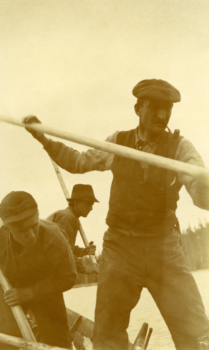 Nærbilde av tre fløtere i aksjon ved Grønåa, stående i båten. 
Fra venstre: Wilhelm Falk (ans. for Staten), Kristian Haugset (16/4 1889 - 1978) og Emil Tannåneset (26/8 1877 - 1960)