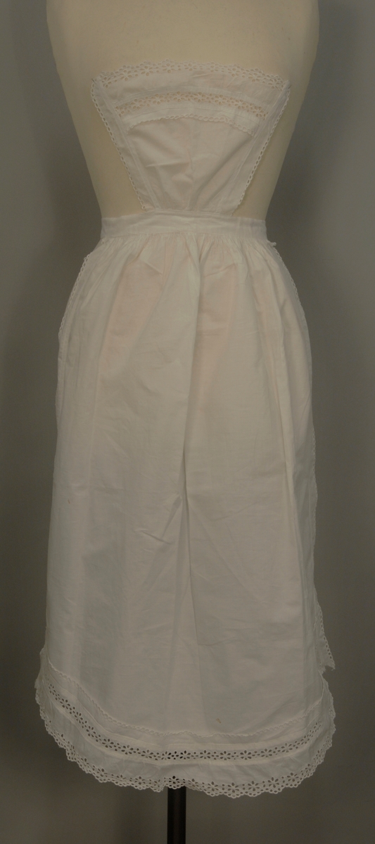 Kvitt (serverings)forkle av staut (lerretsvevd bomullstøy) med blonder. Nedentil er forkleet påsydd en engelsk blonde (4 cm), ovenfor er et mellomverk (2,5 cm) og over der igjen en rad med engelsk blonde og over der en ca 2,5 cm bred remse med stoff med små hull som vender oppover. Samme enkelthullete blonde oppover langs begge sidene. Øverst en liten "lapp" hvor det er samme blondeoppsett som nederst. Forkleet har bånd til å feste rundt livet. Blondene på høyre side (sett forfra) er slitt nederst og litt lengre opp.