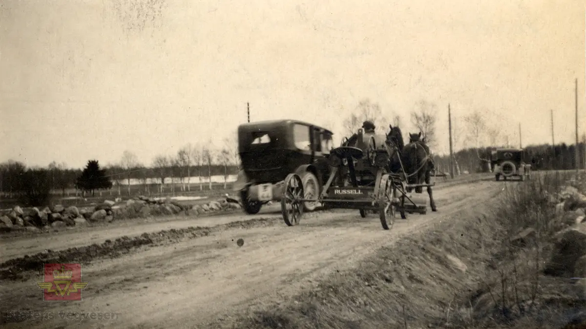 Amerikansk veghøvel "Russel Grader"  i arbeid i Østfold 1924, i følge merking.  Ref. til "Meddelelser fra Veidirektøren", Nr. 47-mai 1924. Artikkel om "Prøve med den amerikanske veihøvel "Russel Grader" samt skrapning av veibanen med "Western" skrape", av overingeniør Thor Olsen. Befaring  med vegdirektoratets og Østfold fylkets ingeniører.  Andre bilder av veghøvelen som er illustrert i artikkelen vises i bildeframvisning 2/5 og 3/5. Bildeframvisning 4/5: "Skraperne av "Western"-typen forarbeides som nævnt ved fylkets verksted og utstyres nu med en fast arm paa den ene side for styring av hele redskapen foruten den bevægelige for stillingen av bladene , som det vil sees av fig. 5". Bildeframvisning 5/5: Vedlikeholdsarbeid med amerikansk vegskrape utføres i Østfold.