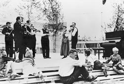 Personer, musikkinstrumenter, bunader, flagg, stol.