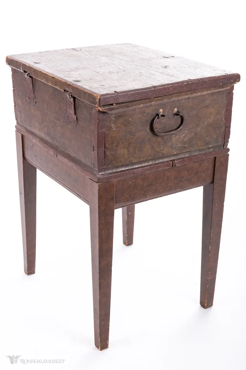 Ensfargede, bølgede dekorfelter midt på og på sidene av lokket, likeså rundt nøkkelhull og ved hjørnene.