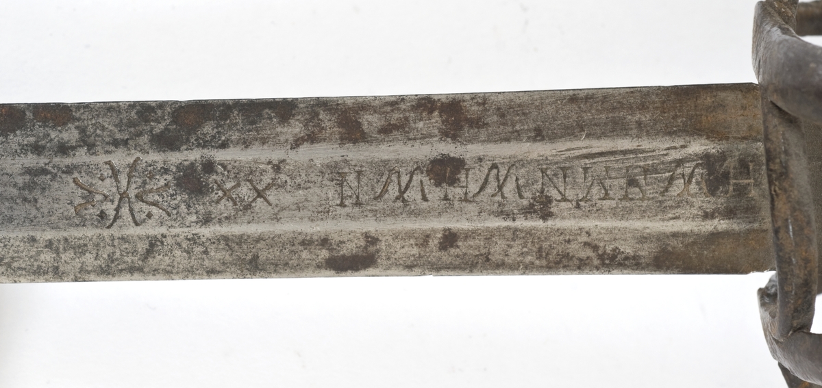 Avleng, plommeformet knapp med nitteknapp. Tregrep med lær bevikling. Asymmetrisk feste med flate bøyler. Fremre parerstang går over i håndbøylen. Sidering. 
Tvenegget, rett klinge med elipseformet tverrsnitt. og 1 kort midtstillt  blodrand på hver side.. Klingen er merket med  Passau-ulv på utsiden og smedmerke på innsiden.