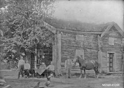 Personer foran bolighus. Hest