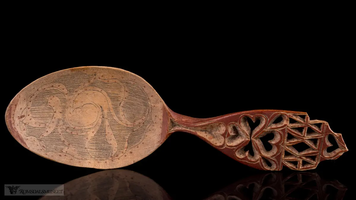 Skaftet perforert,-hjertering, selve skjeen abstrakt flate- og liljemønster med røde prikker.