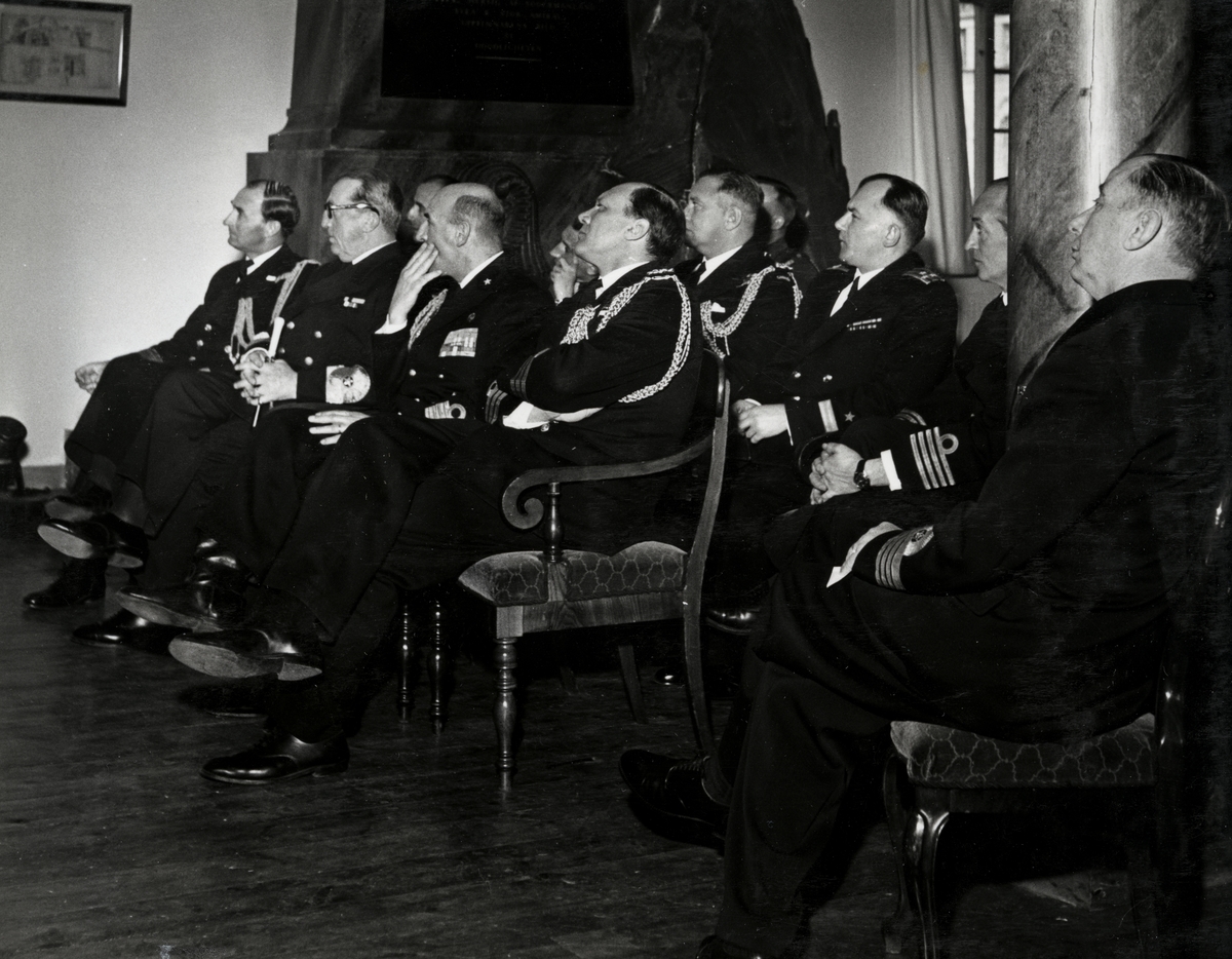 En samling militärer av högre rang sitter i ett rum på stolar uppställda i rader. Samtliga är klädda i uniform. Konteramiral Samuelson syns i bilden som andra personen från vänster. Kommendörkapten Lind af Hageby sitter som andra personen från höger, delvis skymd av en kolonn.
