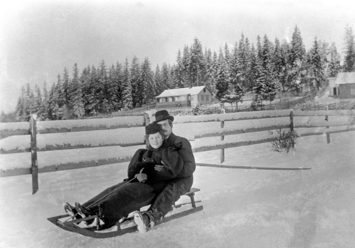 Ingeborg Petersen (datter av overlærer K. Petersen) og vennen Erling på skikjelke i Stafsbergveien, Hamar. Langs skigarden i bakgrunnen går i dag Ringgata. Vinter. 