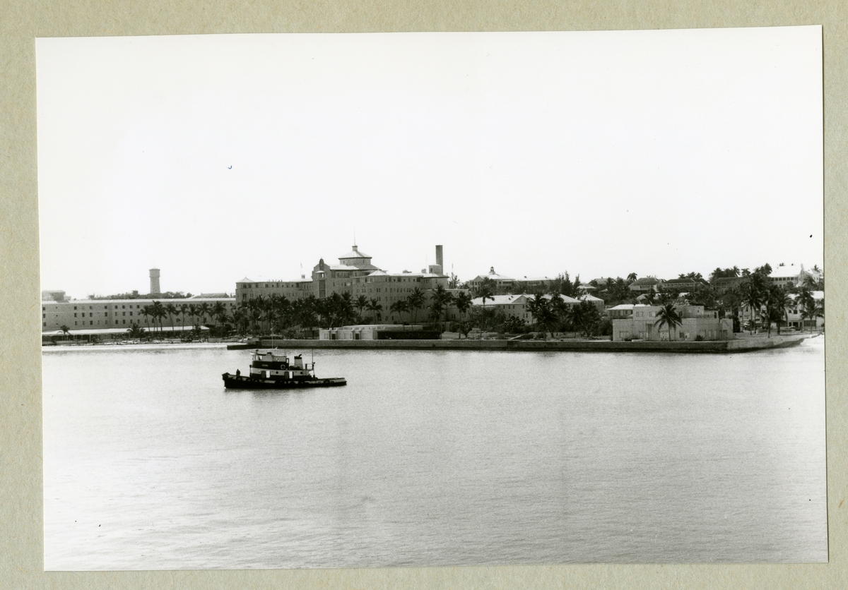Bilden föreställer en stadsvy av Bahamas huvudstad Nassau med bebyggelse och växtlighet. Framför staden syns ett fartyg. Bilden är tagen under minfartyget Älvsnabbens långresa 1966-1967.
