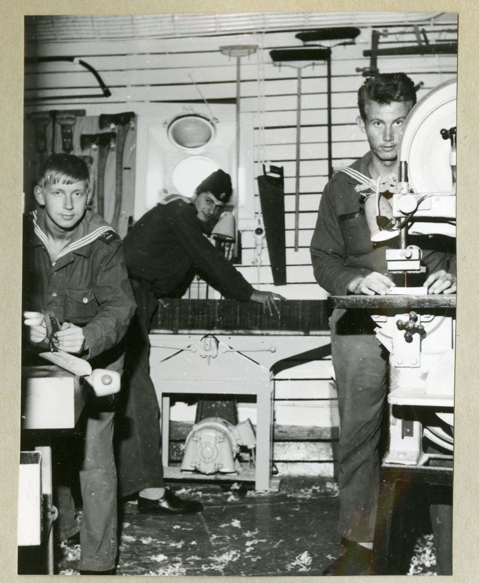 Bilden föreställer tre uniformsklädda besättningsmän i arbete i snickarverkstaden ombord på minfaryget Älvsnabben under långresan 1966-1967.  Mannen till höger bakom sågen är Sture Ohm.