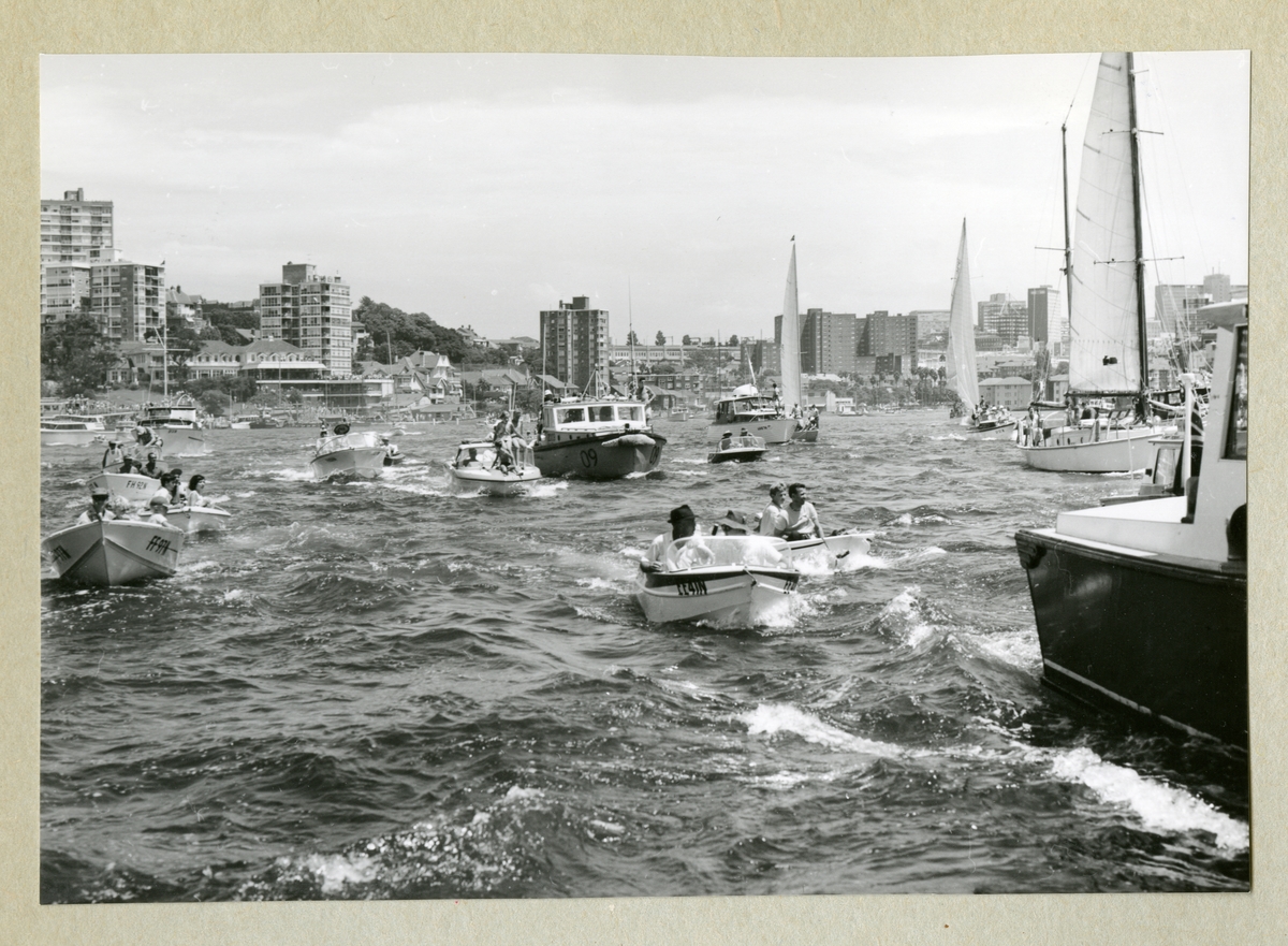 Bilden föreställer en samling av motor- och segelbåtar av olika storlekar. I bakgrunden syns kanten av en kuststad med höghus längs med kustlinjen. Bilden är tagen under minfartyget Älvsnabbens långresa 1966-1967.