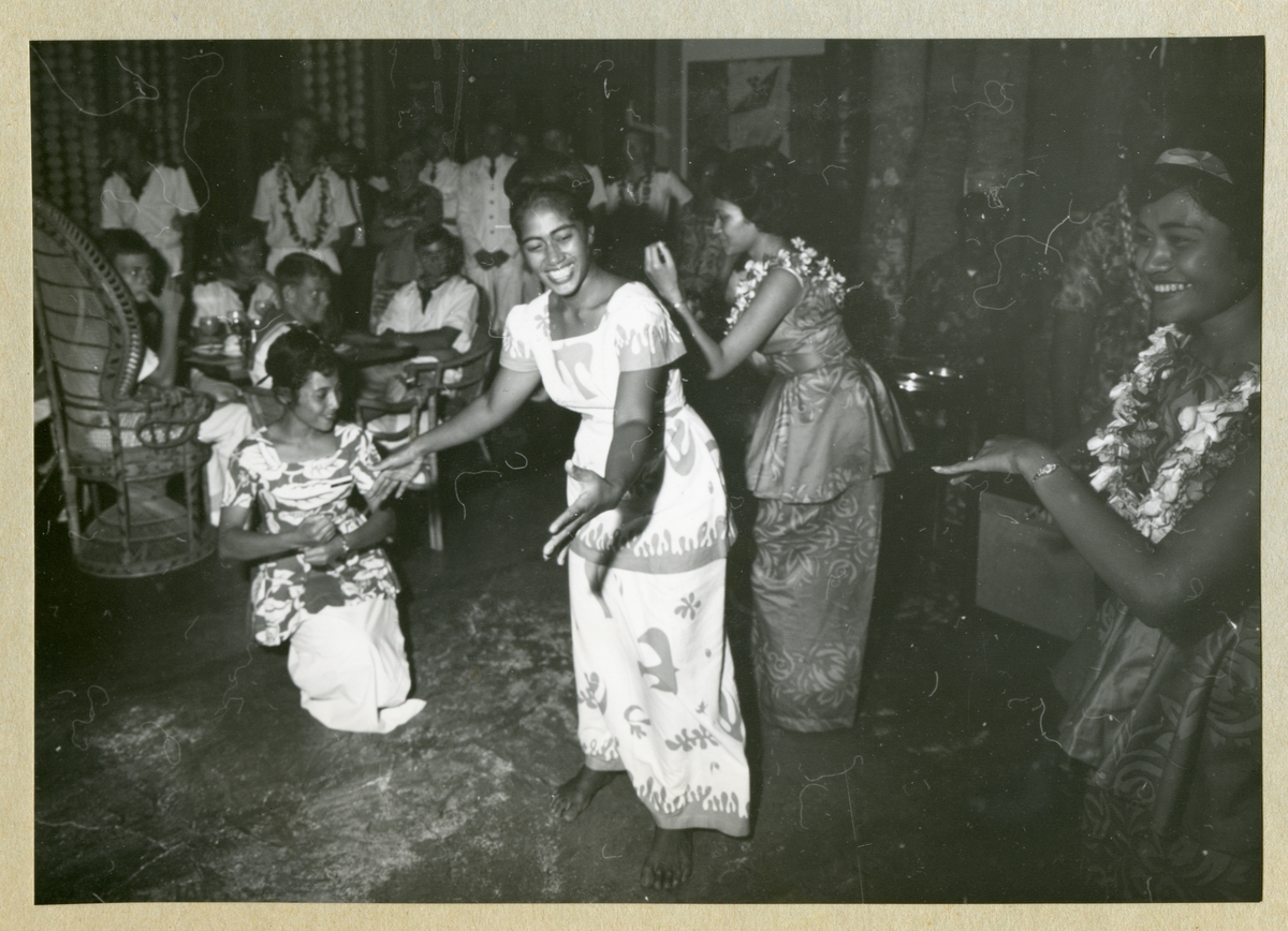 Bilden föreställer fyra kvinnor som framför en dans. I bakgrunden syns uniformsklädda män som åskådare. Bilden är tagen i Samoa i samband med minfartyget Älvsnabbens långresa 1966-1967.