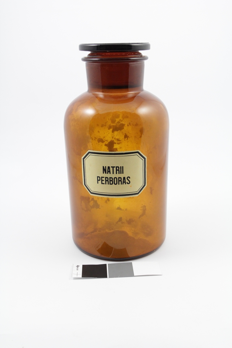 Standglass med propp, vid hals, brun. Brukes til pulver. Pulveret (Natrii perboras) ble brukt til produksjon av legemiddler.