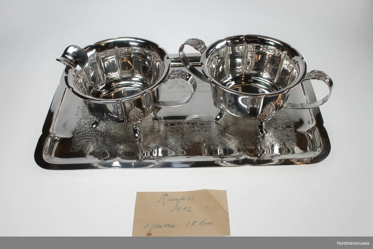 Fløtesett som består av et brett, en sukkerkopp og en fløtemugge i sølvplett. Brettet har innrisset dekor i bunnen. Sukkerkopp og fløtemugge har 4 føttet og hank. Dekor over hver fot og øverst på hanken. En løs papirlapp med påskrift "Raufoss 1952 1. premie 17 km " ligger på brettet.