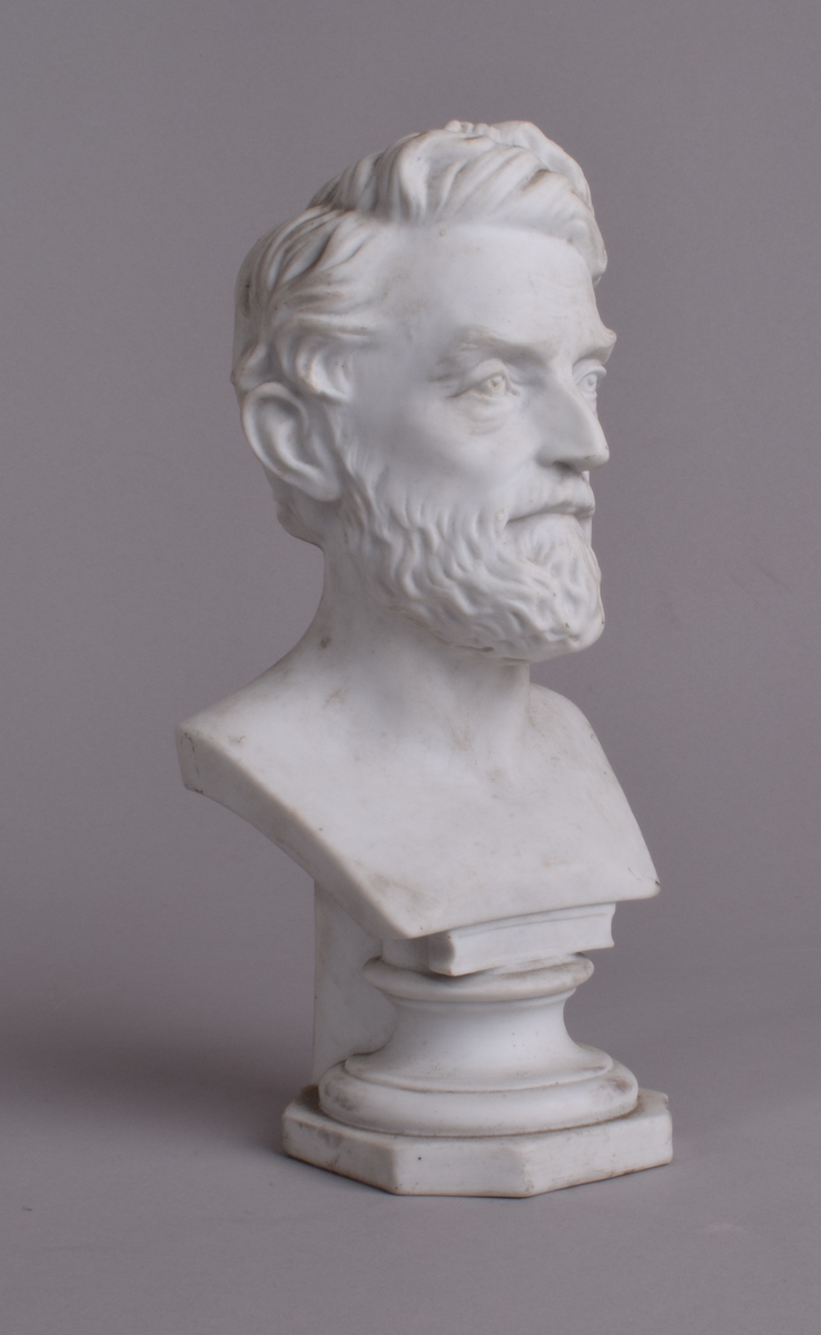 Liten byste av mann med skjegg på åttekantet sokkel.