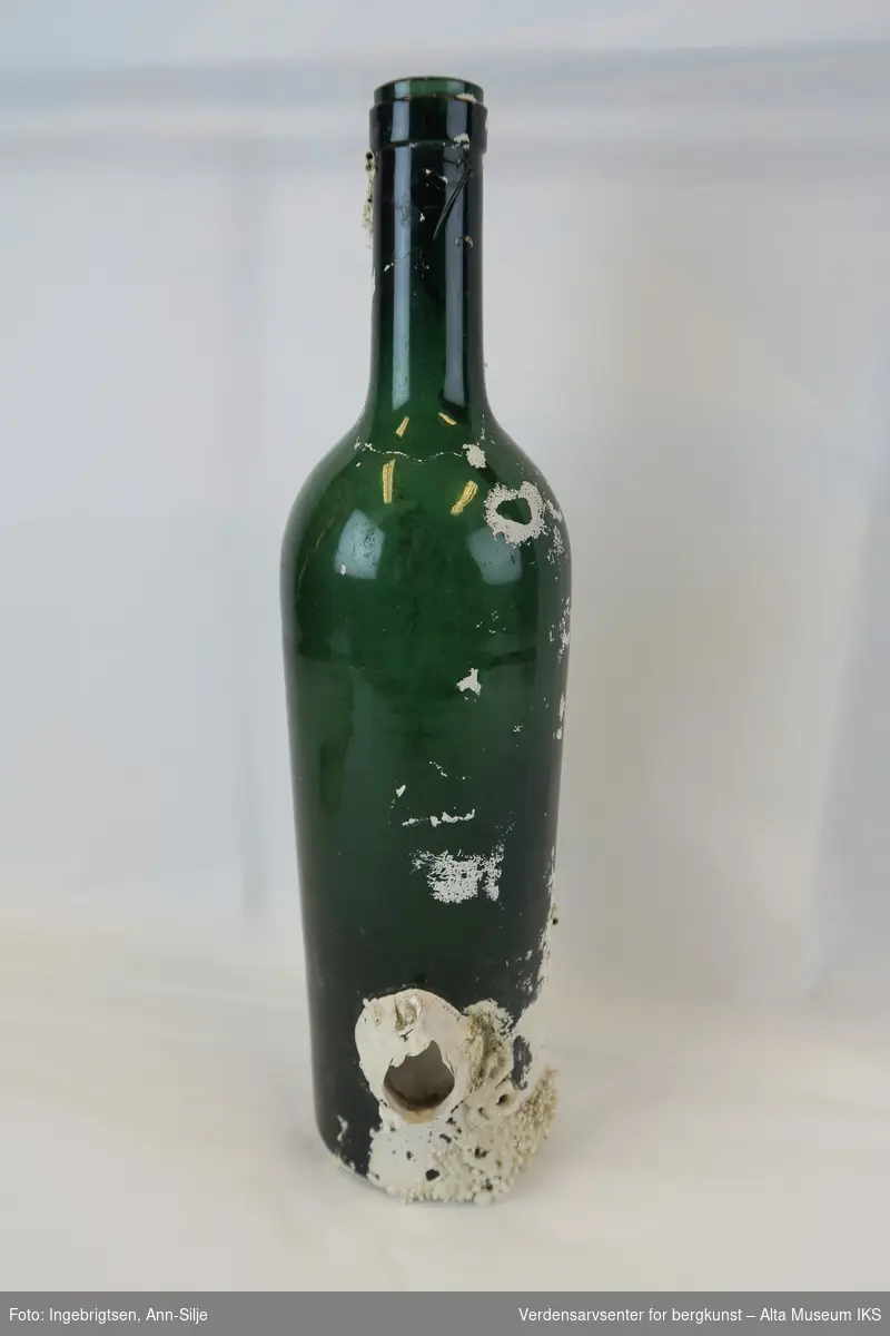 Form: Vanlig grønn vinflaske. På flaska er det grodd kalkalger, særlig rundt bunnen.