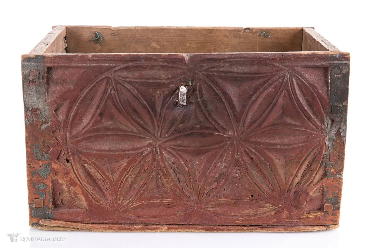 To sammenkomponerte seksbladsrosetter på hver langside. På kortsidene er det skåret ut fire klokkeformede strukturer fylt med spetter og border som til sammen ligner på et noe asymmetrisk solkors/kors.